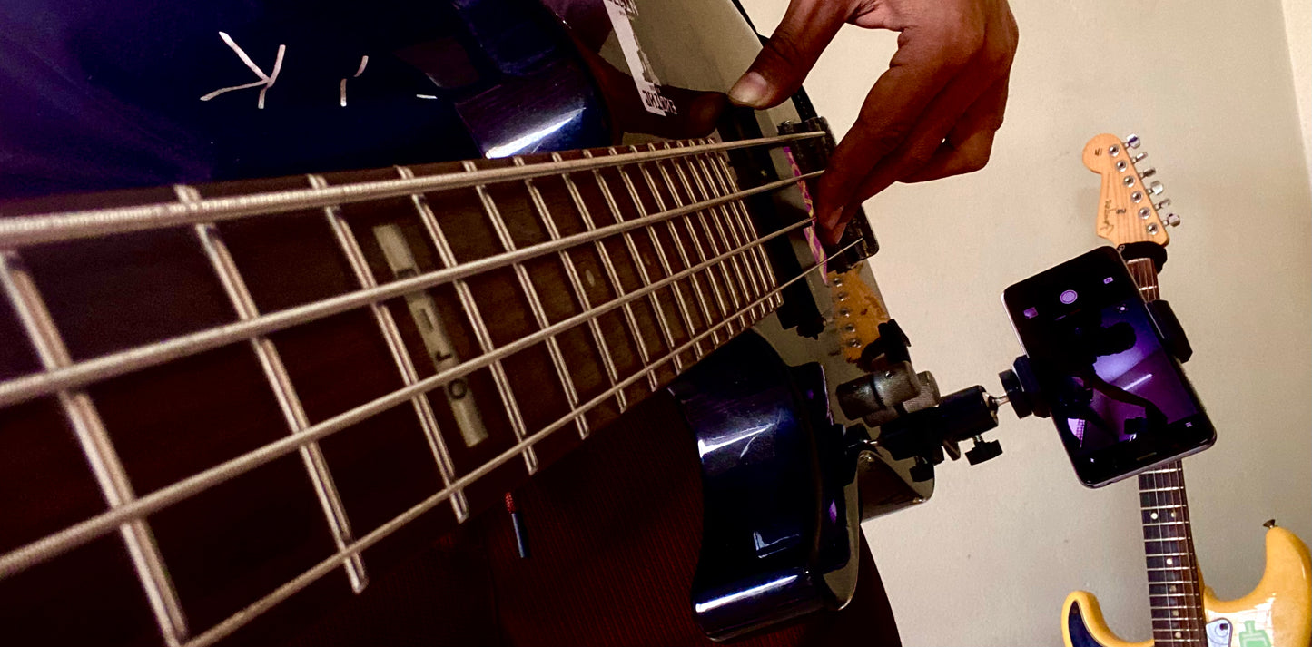 A low-angle POV shot of a musician playing a guitar, with the 360-degree phone mount attached to the body to capture close-up footage of the strings and fretboard.