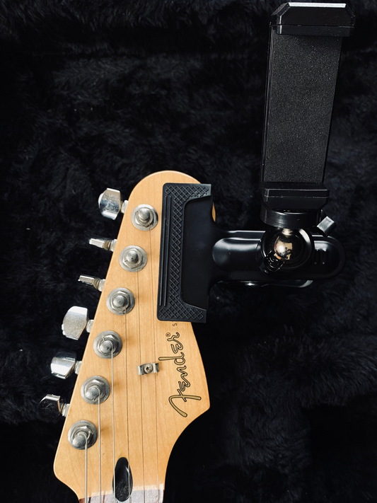 Universal guitar headstock phone holder mount with 360-degree rotation attached to a Fender electric guitar for recording POV video and reading tabs.